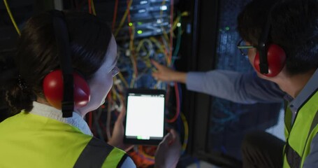 Diverse female and male it technicians wearing headphones using tablet checking computer server