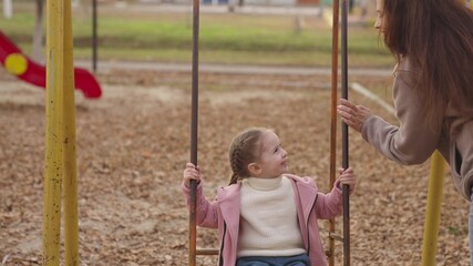 little kid swinging on a swing and laughing while flying up, an autumn playground, a happy family, a mother rolls child in city park, childhood dream to fly, smile at mom on a walk, play with a baby