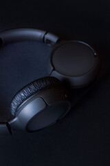 modern black wireless headphones with bluetooth system, on textured black background, vertical format
