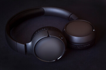 modern black wireless headphones with bluetooth system, on black textured background
