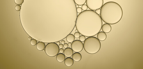A creative pattern produced by oil droplets to water leading to the formation of a mass of different sized circular bubbles highlighted by the addition of pale golden lighting effects background.
