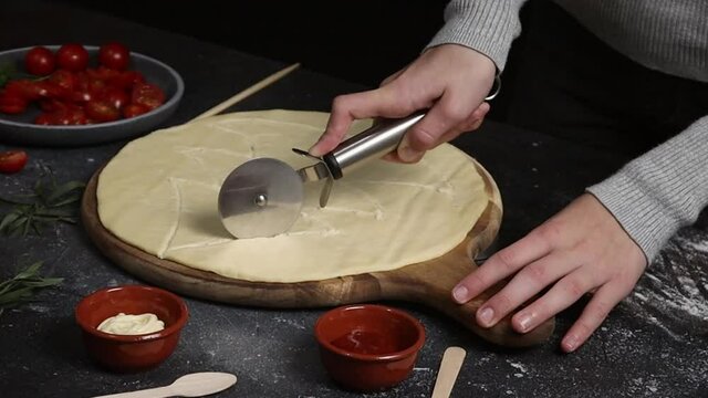 A little girl cuts a Christmas tree homemade pizza dough with a knife on a cutting board on a dark table, close-up side view. Family fun and cooking concept.