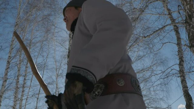 Man dressed in traditional Mongolian clothing deel walking in a forest.