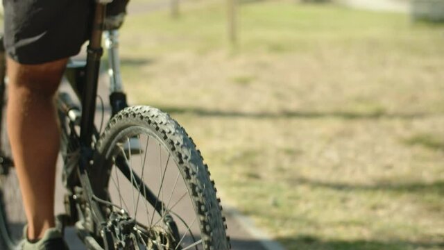 Close-up shot of man with bionic leg riding bike in summer park. Back view of unrecognisable male person in shorts riding bicycle along greenway on weekends, Disability, sport concept 