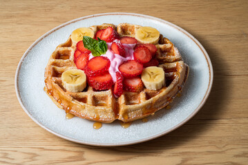 waffles on white plate, with strawberries, banana, honey and mint leaf