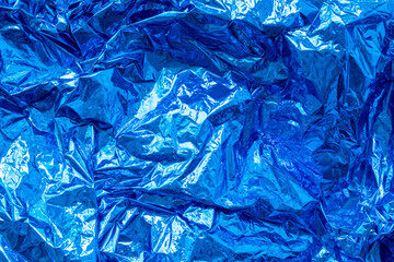 Blue crumpled, creased iridescent metal foil texture. Abstract colored background. Shiny monochrome surface.