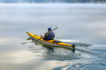 Fototapeta na wymiar Lone kayaker in autumn paddling on Lake McDonald, Glacier National Park, Montana on a foggy morning