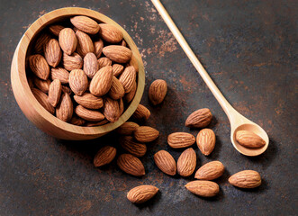 Almond top view on old dark vintage style background. Almonds in a wooden bowl and a wooden spoon and nuts are laid freely. Healthy food and snacks organic vegetarian food.