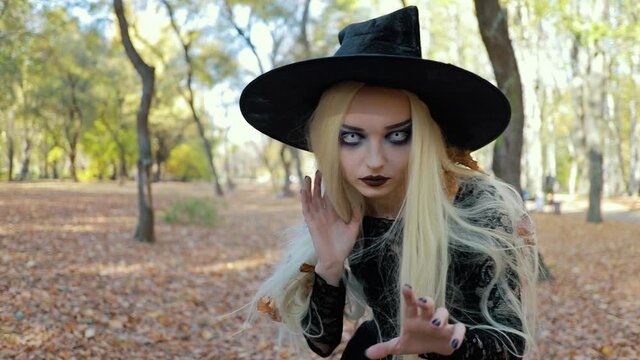 Portrait of a scary evil witch in the autumn forest with a black top hat on her head looks at the camera. Halloween horror concept. Death look.