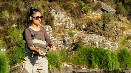 A young asian female fly fishing on a river on a summers evening - obrazy, fototapety, plakaty