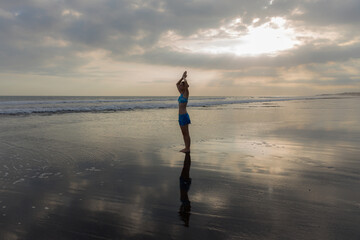 Yoga on the beach during sunset. Slim woman practicing yoga. Standing asana. Hands raised up in namaste mudra. Water reflection. Yoga retreat. Healthy lifestyle. Copy space.