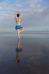 Yoga pose. Vrikshasana asana. Young woman practicing tree pose at the beach near the ocean during...
