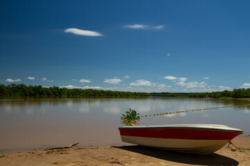 View of the river beach in a summer sunny day. A boat in the sand in the foreground and the tropical jungle in the background reflected in the water.