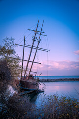 The wreckage of La Grande Hermine, a relica carrack, lies abandoned and rotting in the water of Jordan Harbour near St. Catherines, Ontario during sunset.