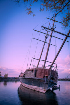 The wreckage of La Grande Hermine, a relica carrack, lies abandoned and rotting in the water of Jordan Harbour near St. Catherines, Ontario during sunset.