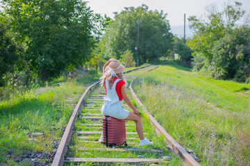 tired traveler sits on the railroad on a red suitcase