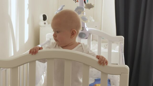 Cute smiling baby boy standing in cot at home, happy kid having fun learning to stand up in baby cot. High quality 4k footage