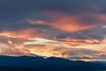 Pink aesthetic sunset vibes in fall, autumn with snow capped mountains in the distance and heavy, thick cloud cover. 