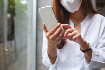 Closeup of a woman wearing protective face mask, holding and using mobile phone for Healthcare and Coronavirus concept