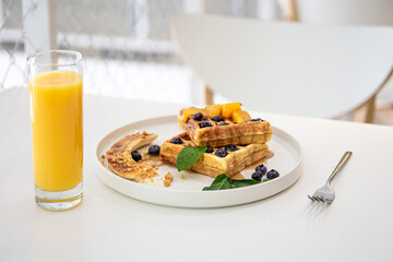 Delicious Belgian waffles with berries and fruits and a glass of juice.