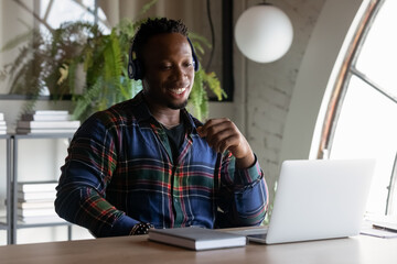 Smiling pleasant young african american employee worker manager wearing headphones, holding distant video call meeting on computer, improving professional knowledge on online courses, virtual event.