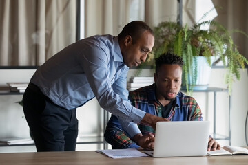 Skilled smart middle aged african ethnicity leader ceo executive manager coaching new biracial employee, explaining corporate computer software applications in modern office, cooperation concept. - Powered by Adobe