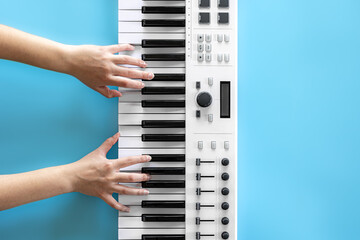 Fototapeta na wymiar Female hands play musical keys on a blue background, top view.