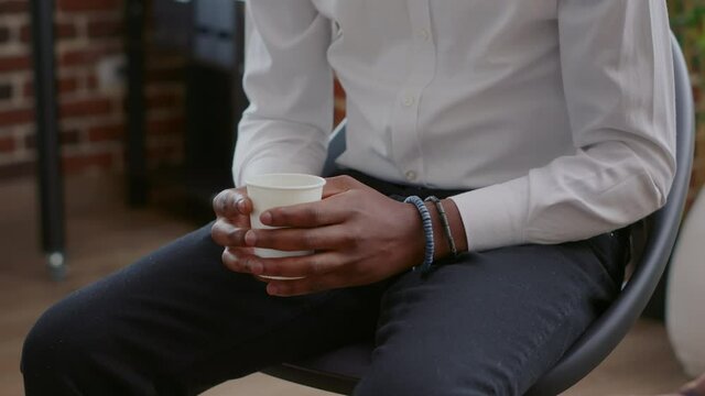 Close up of african american man fewling nervous while holding cup of coffee at aa meeting. Adult with anger management issues having hot drink in hands, attending therapy session.