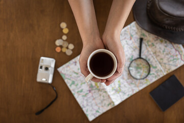 Fototapeta na wymiar Flat lay, map, magnifier, documents and a cup of coffee in the hands of a woman.