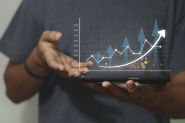 Business man holding tablet and showing holographic graphs and stock market statistics gain profits. Concept of growth planning and business strategy. Display of good economy form digital screen.