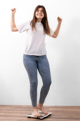 Obraz premium Happy girl is weighed on the scales at home, the joy of losing weight.