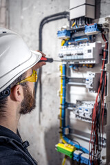 A male electrician works in a switchboard with an electrical connecting cable.