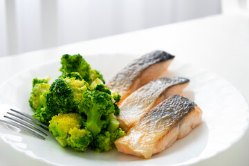 Roasted salmon fish and boiled broccoli on white plate with fork. Healthy eating and dieting. Easy recipe of Mediterranean seafood cuisine of fish and vegetables.