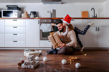 Father and daughter decorate christmas gifts at home. Daughter hugs father in santa hat. Christmas...