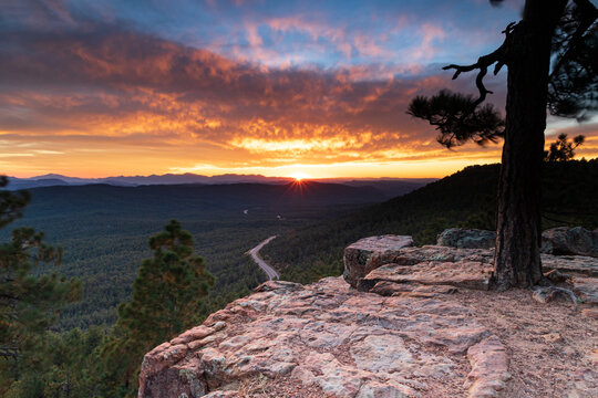 Arizona sunset, from the top of Mogollan Rim above Payson. Pine forest and highway below; Sunburst, brillian orange clouds and blue sky in distance. 
