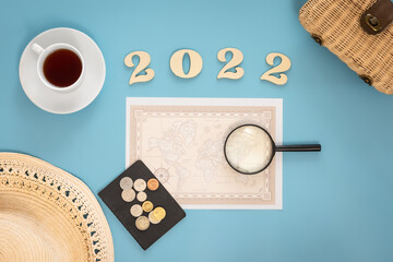 Travel flat lay composition with world map and numbers 2022 on blue background.