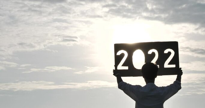 silhouette of a person holding a sign with year number 2022, 2022 year symbol with sunset, happy new year 2022 concept