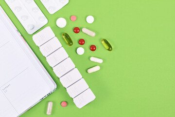 Pills, capsules, pill box and calendar on side of green background with copy space