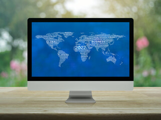 Start up business flat icon with global words world map on desktop modern computer monitor screen on wooden table over blur pink flower and tree, Happy new year 2022 global business start up online co