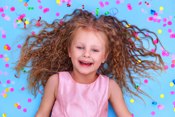 little girl laughs rejoices on a blue background with confetti top view birthday celebration concept