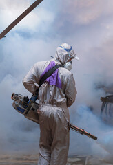 Rear view of healthcare worker using fogging machine spraying chemical to eliminate mosquitoes...