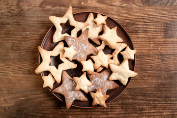 Homemade cookies in form of stars on brown plate in center of rustic brown wooden background. - Powered by Adobe