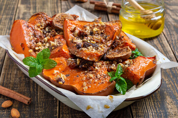 Baked pumpkin slices with nuts, honey and dried fruits on a wooden background. Close-up. Proper nutrition, dietary meal. Vegetables nutritional value concept.
