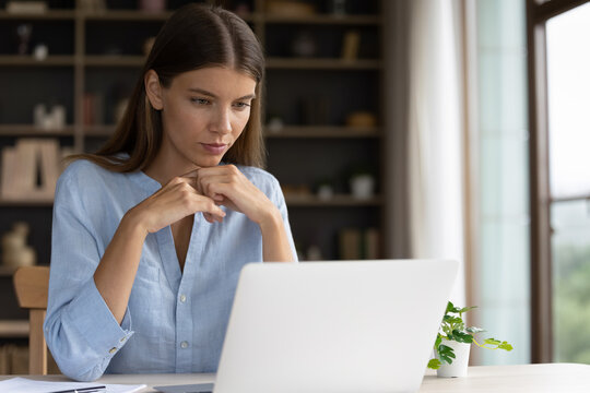 Thoughtful concentrated millennial business woman looking at computer screen, considering project problem solution, analyzing marketing data, watching educational video studying at home office.
