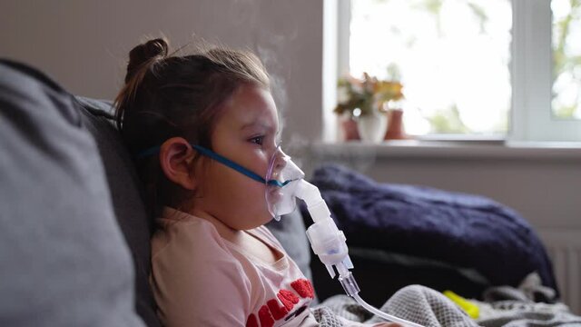 Sick adorable preschool girl with nebuliser mask at home. Treatment for bronchitis with inhaling medicine nebula.