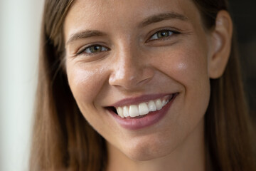 Fototapeta premium Close up head shot beautiful young woman with perfect skin looking at camera, showing whitening smile with healthy straight teeth, feeling satisfied with professional dental or cosmetology procedure.