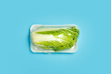 Vegetables in plastic packaging from the supermarket are minimal. Chinese cabbage in cellophane and non-degradable plastic on a blue background. Biodegradable product packaging, environmental