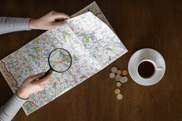 Map and magnifier in female hands on a wooden background, top view.