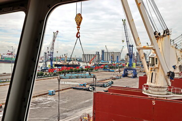 Cargo terminal for unloading steel plates from bulk carrier by ships cranes. View of the pier, cranes and various equipment. Port of Surabaya. Indonesia, January, 2021.