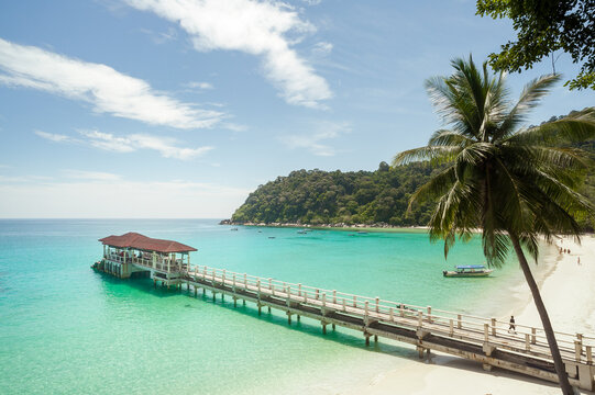 A sunny beach, palms and a pier in turquoise waters in Malaysia.